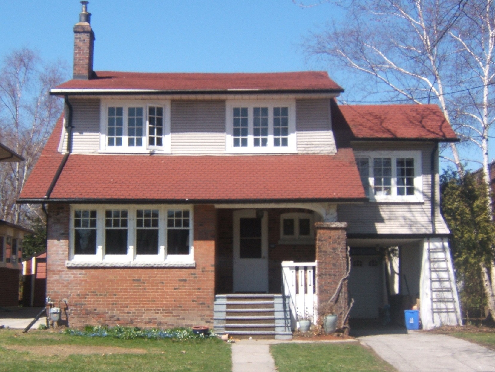 Brick bungalow-style house with a covered front porch, red roof and front steps beside a birch tree