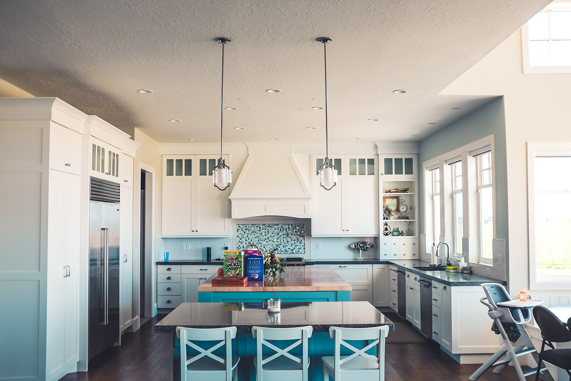 Bright white kitchen with blue island, pendant lights, open shelving and large windows