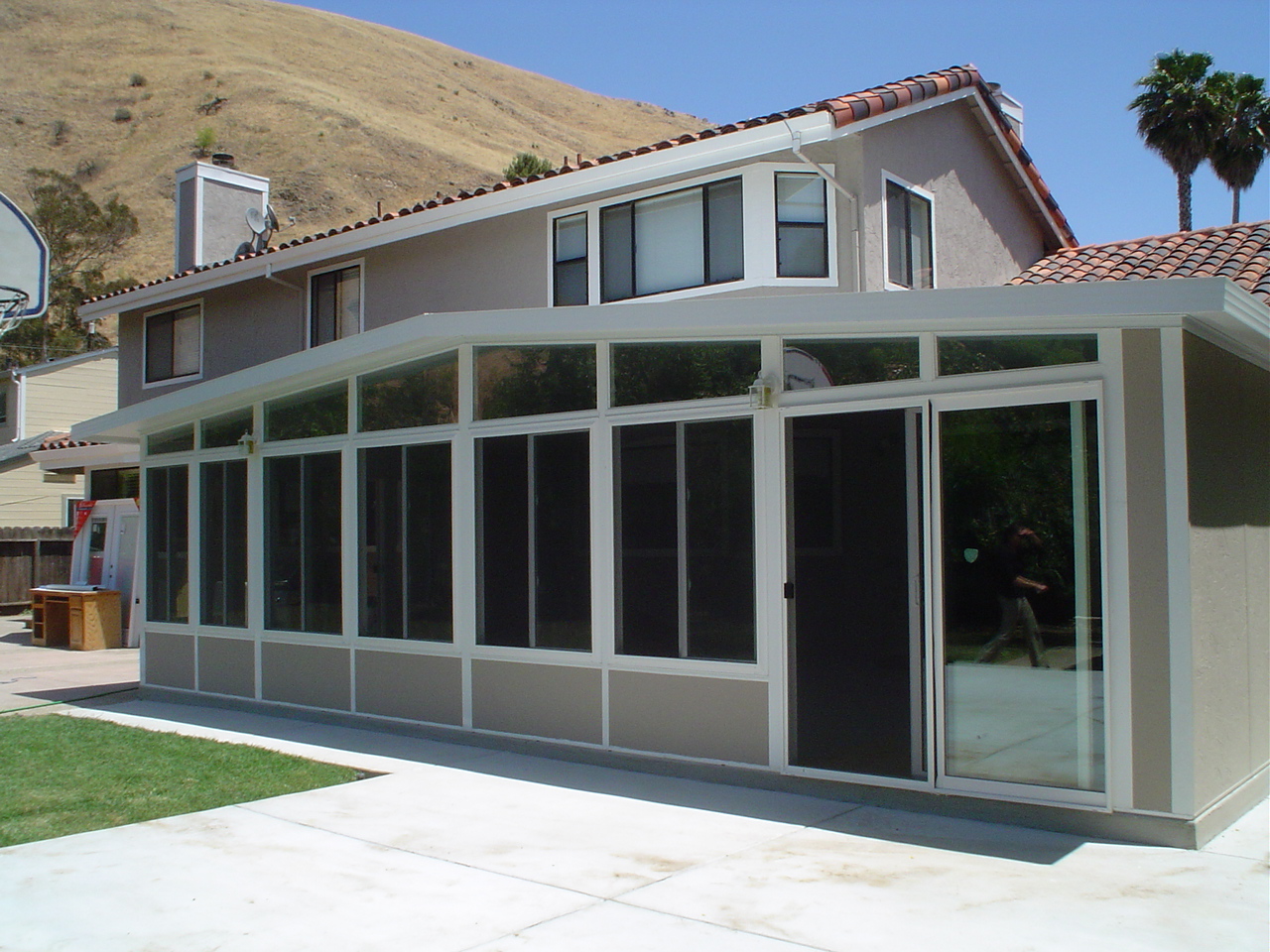 Gable-roofed sunroom addition with floor-to-ceiling windows attached to the back of a house