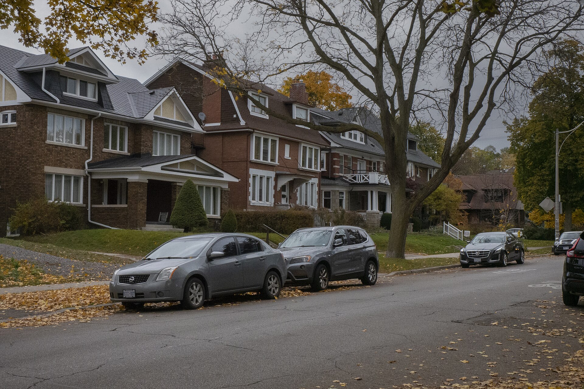 Row of older brick houses with front porches and gables along a leafy street near High Park in Toronto