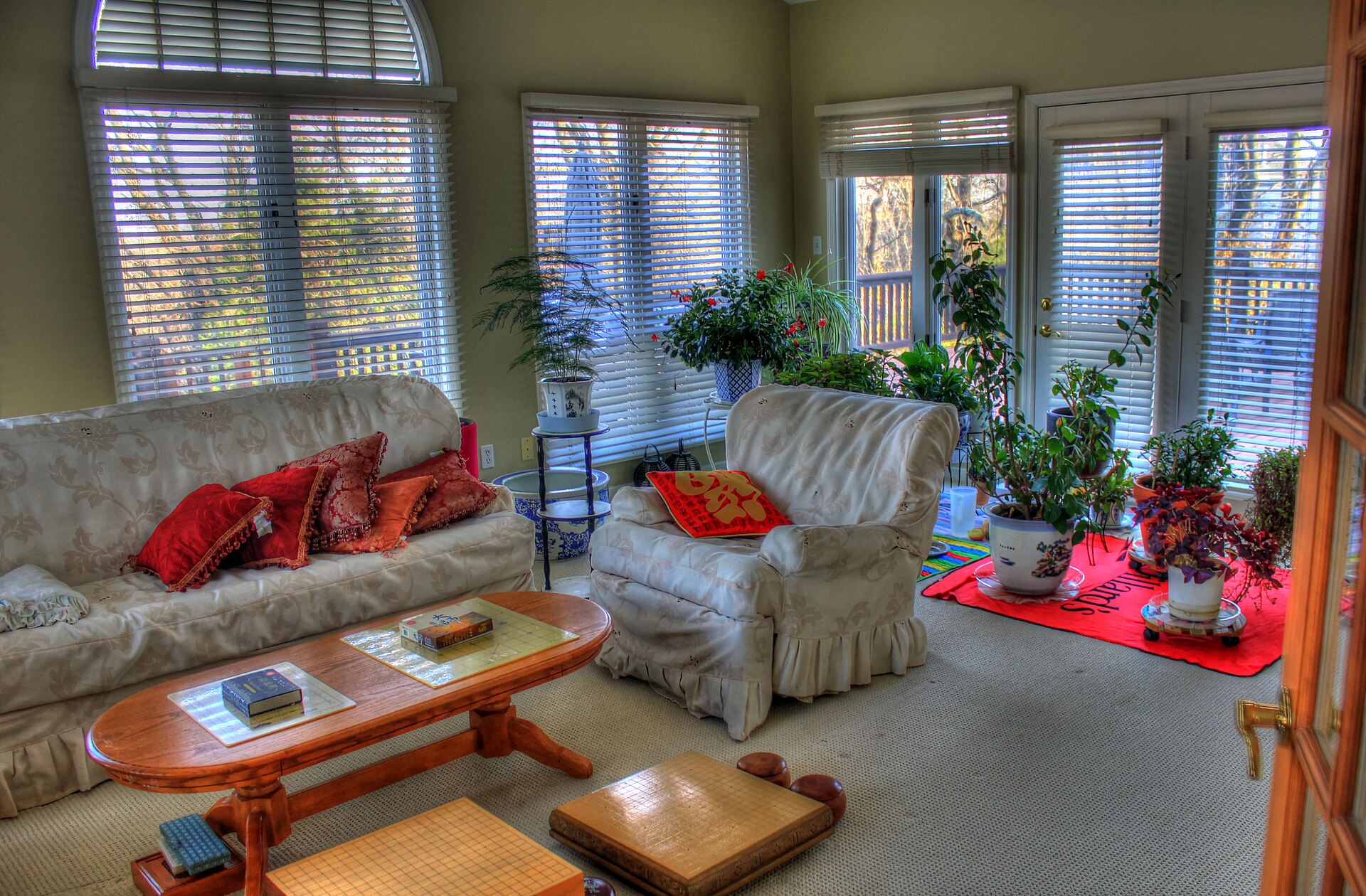 Sunroom interior with a sofa, armchair, coffee table and potted plants beside walls of windows