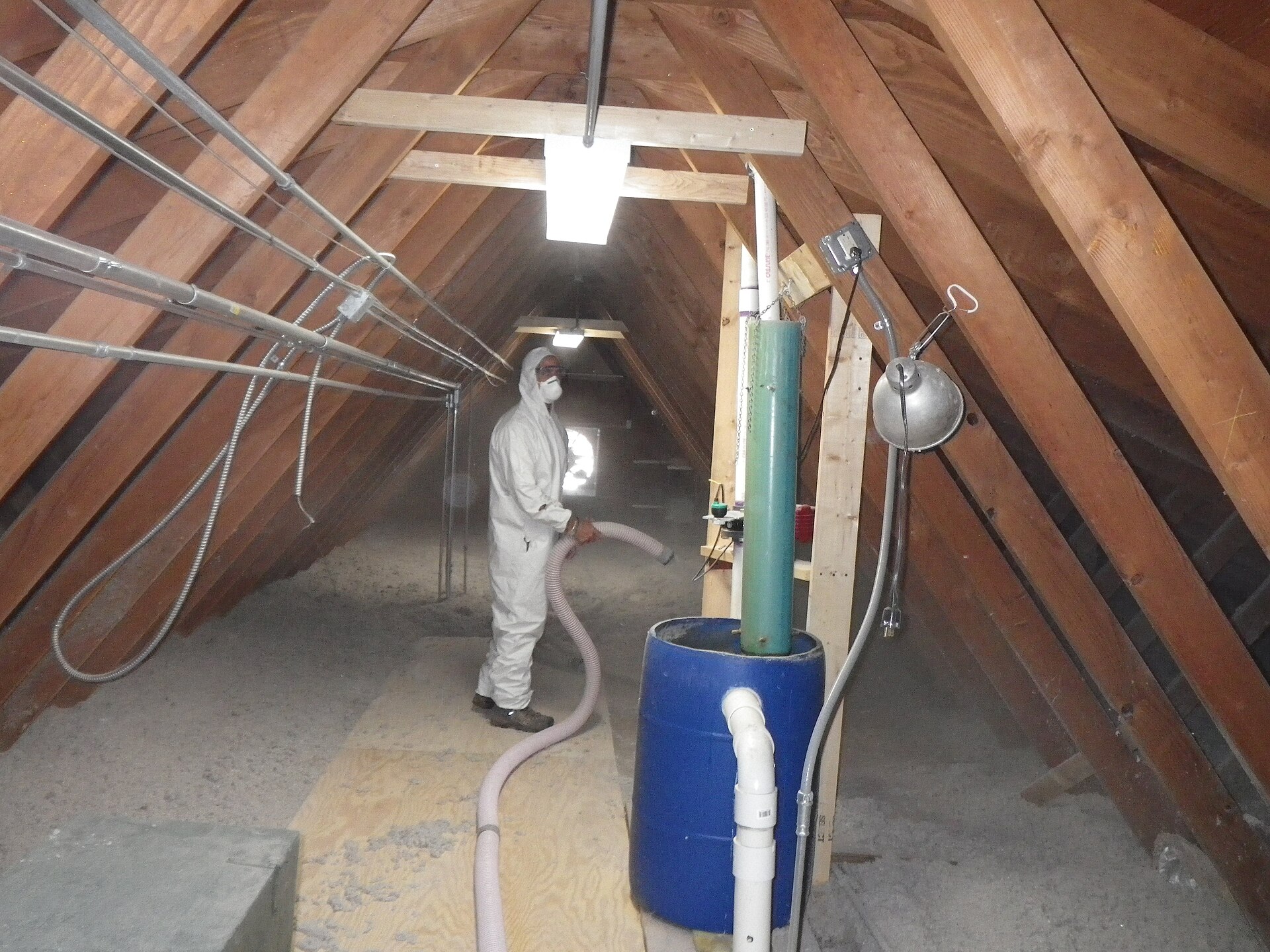 Worker in a white protective suit blowing loose-fill cellulose insulation into an attic with a hose