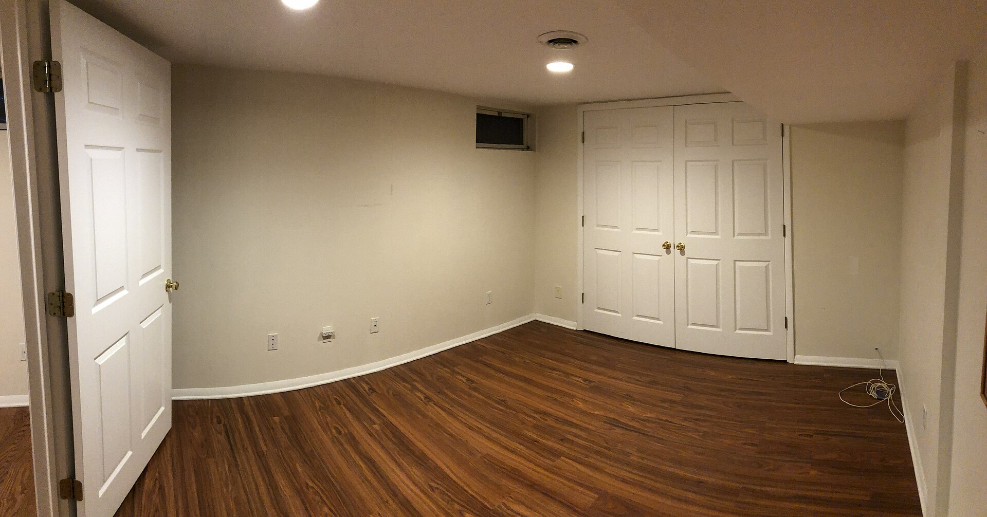 Empty finished basement bedroom with hardwood floor, white walls, pot lights and closet doors