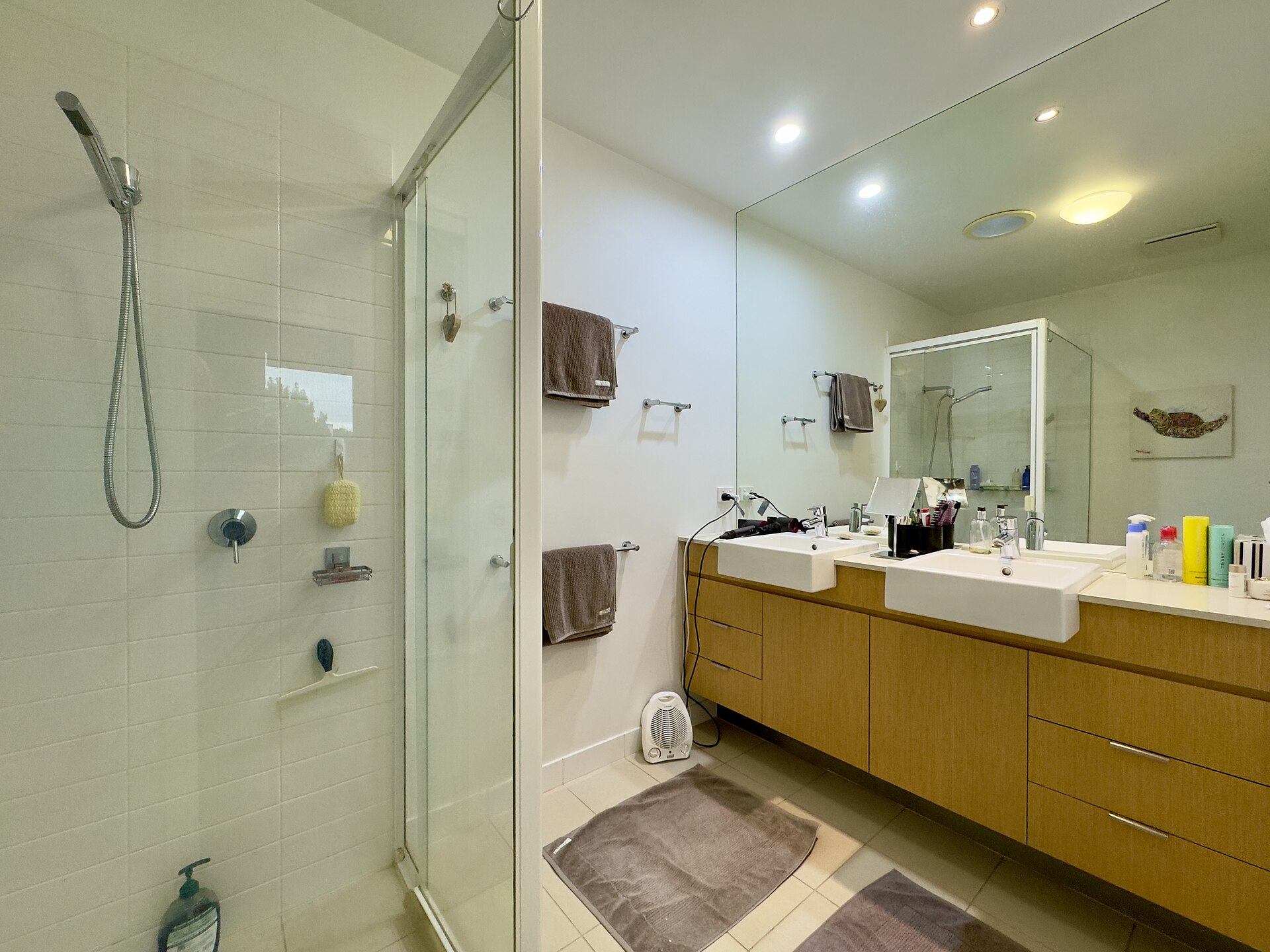 Modern bathroom with a frameless glass walk-in shower beside a long wood double vanity and mirror