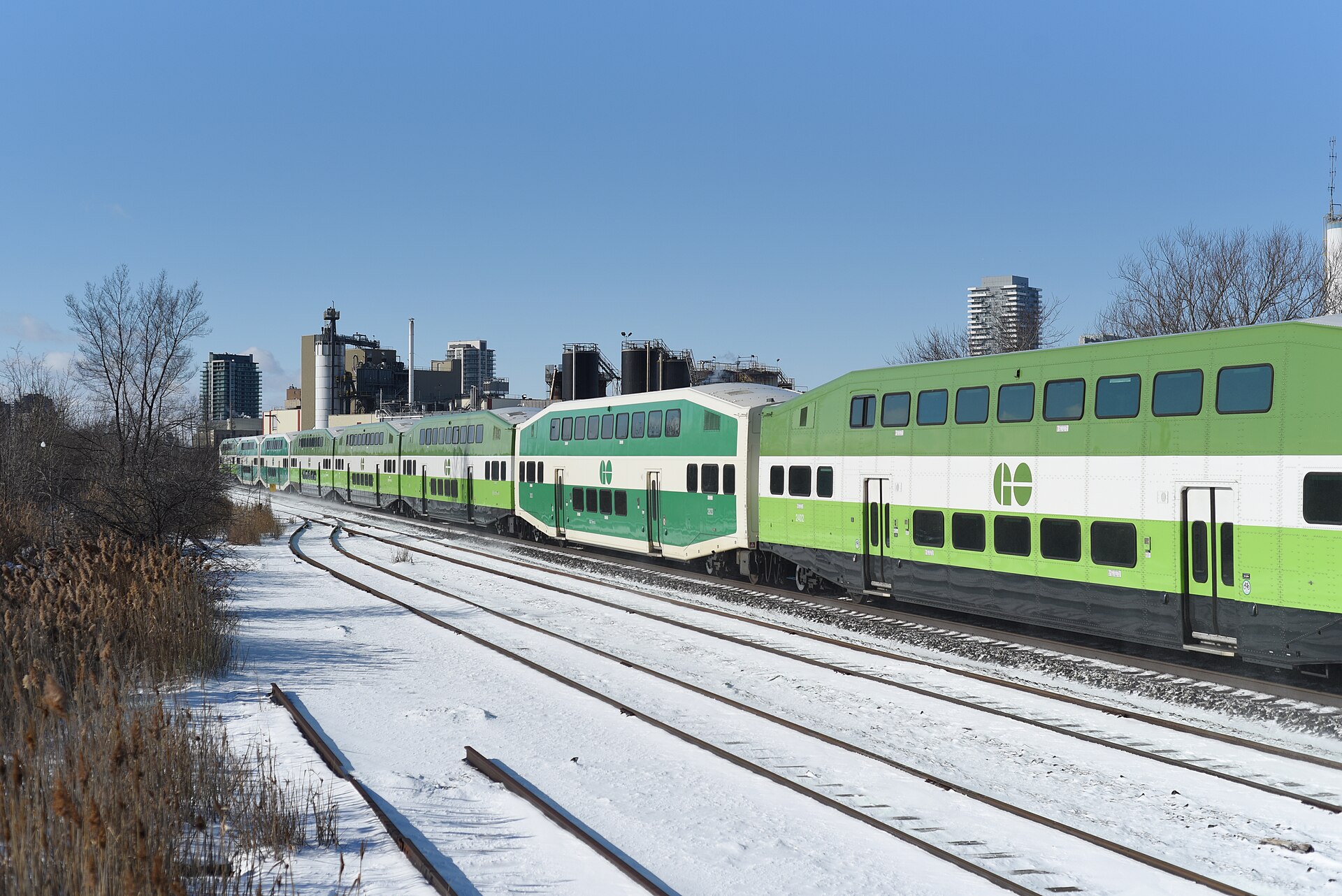 GO Transit commuter train running past snowy tracks and low-rise buildings in Brampton on a sunny winter day