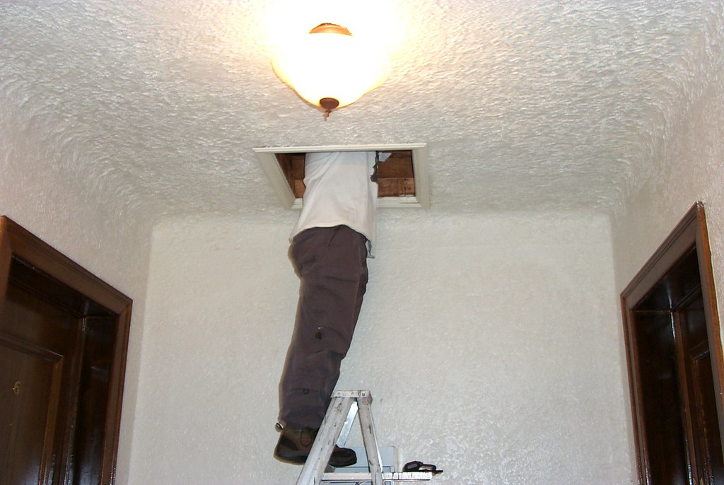 Home inspector on a stepladder climbing through a ceiling hatch into the attic of a house