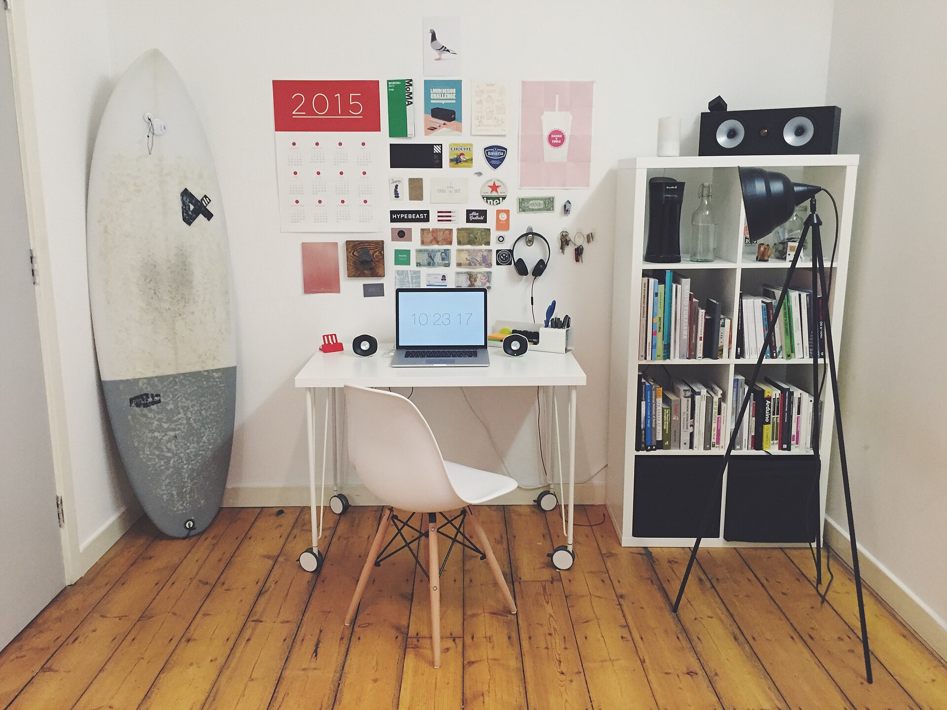 Small home workspace with a white desk, laptop, chair and bookshelves against a white wall