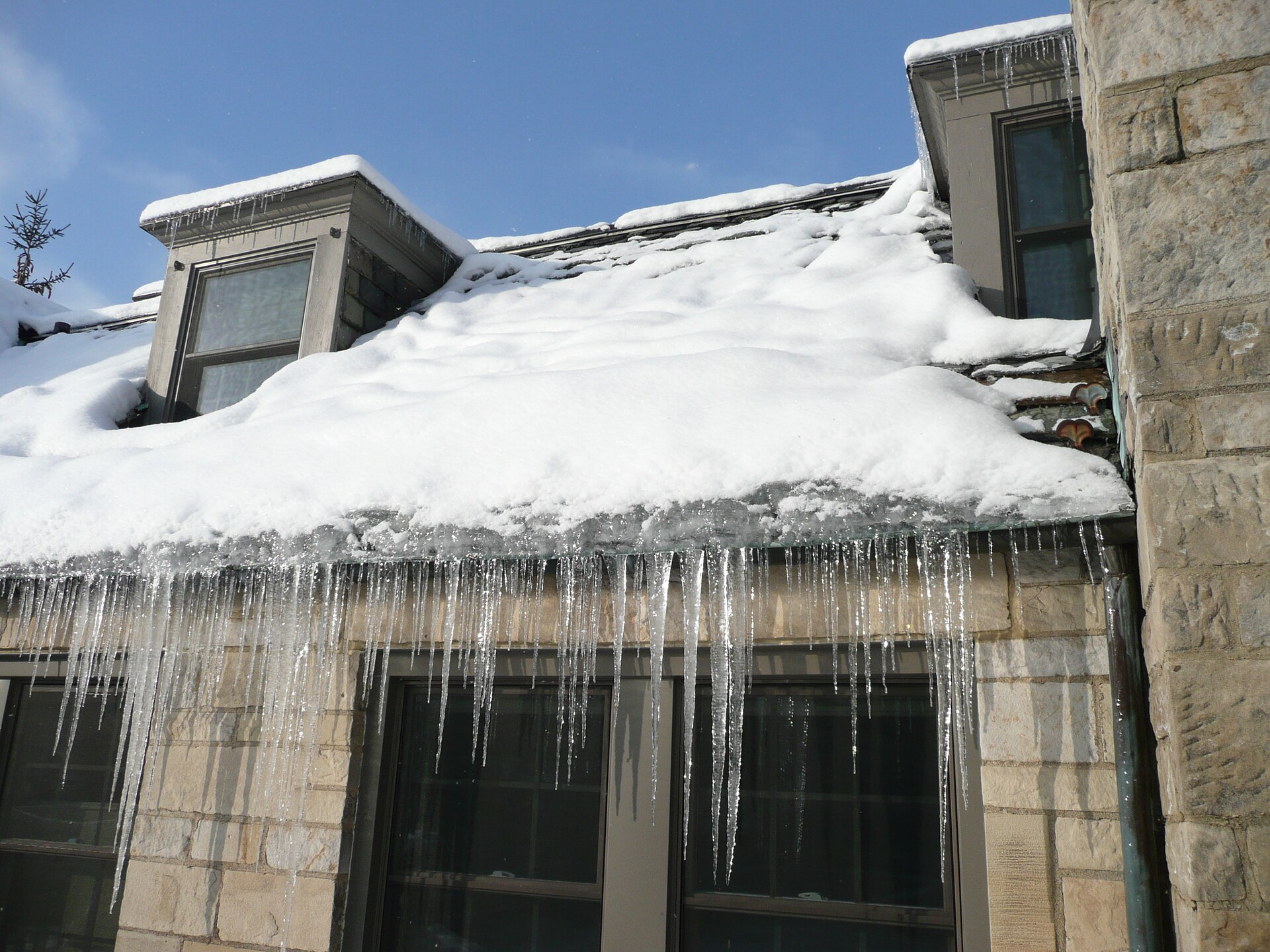 Thick snow on a roof edge with a ridge of ice and long icicles hanging from the eaves