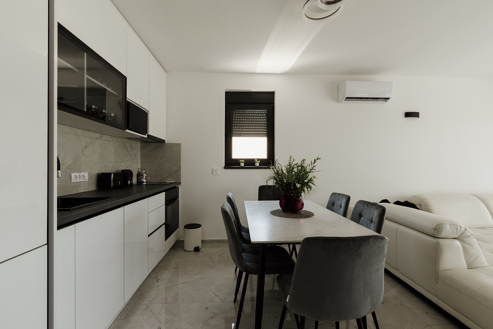 White galley-style kitchen opening onto a dining table and a white sofa in one bright room