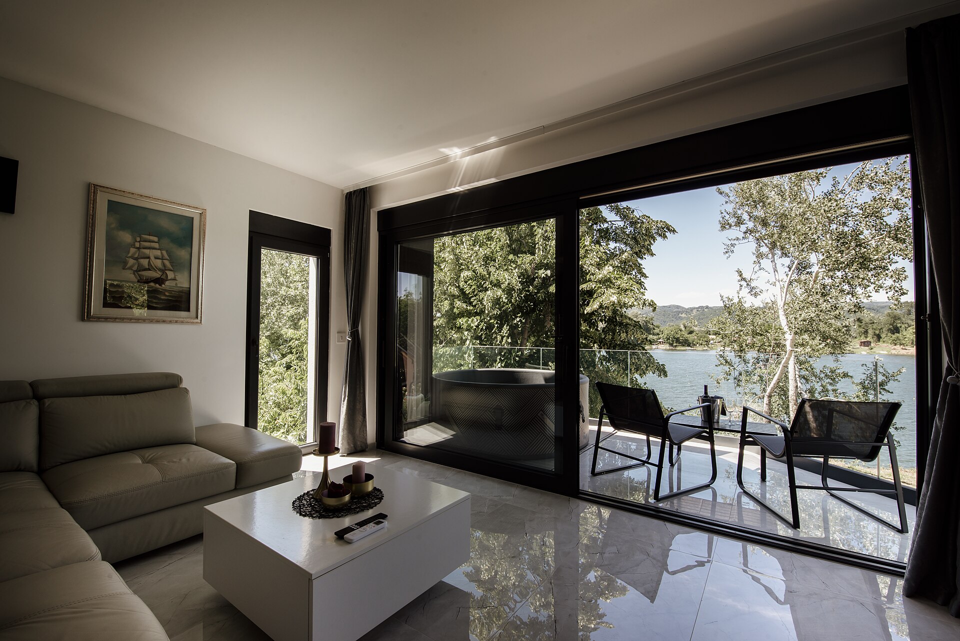 Living room with a cream sofa facing large sliding glass doors that open to a balcony, trees and a lake