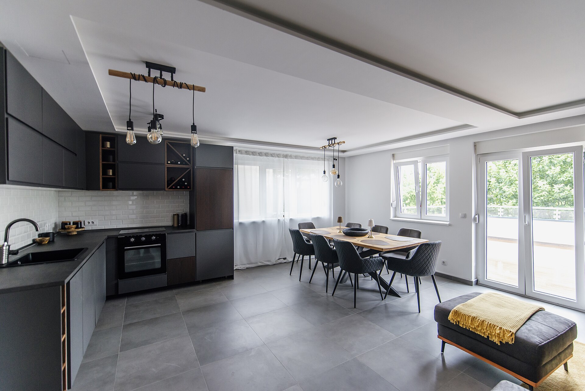 Open-plan kitchen with dark cabinets flowing into a dining table and seating area lit by large windows