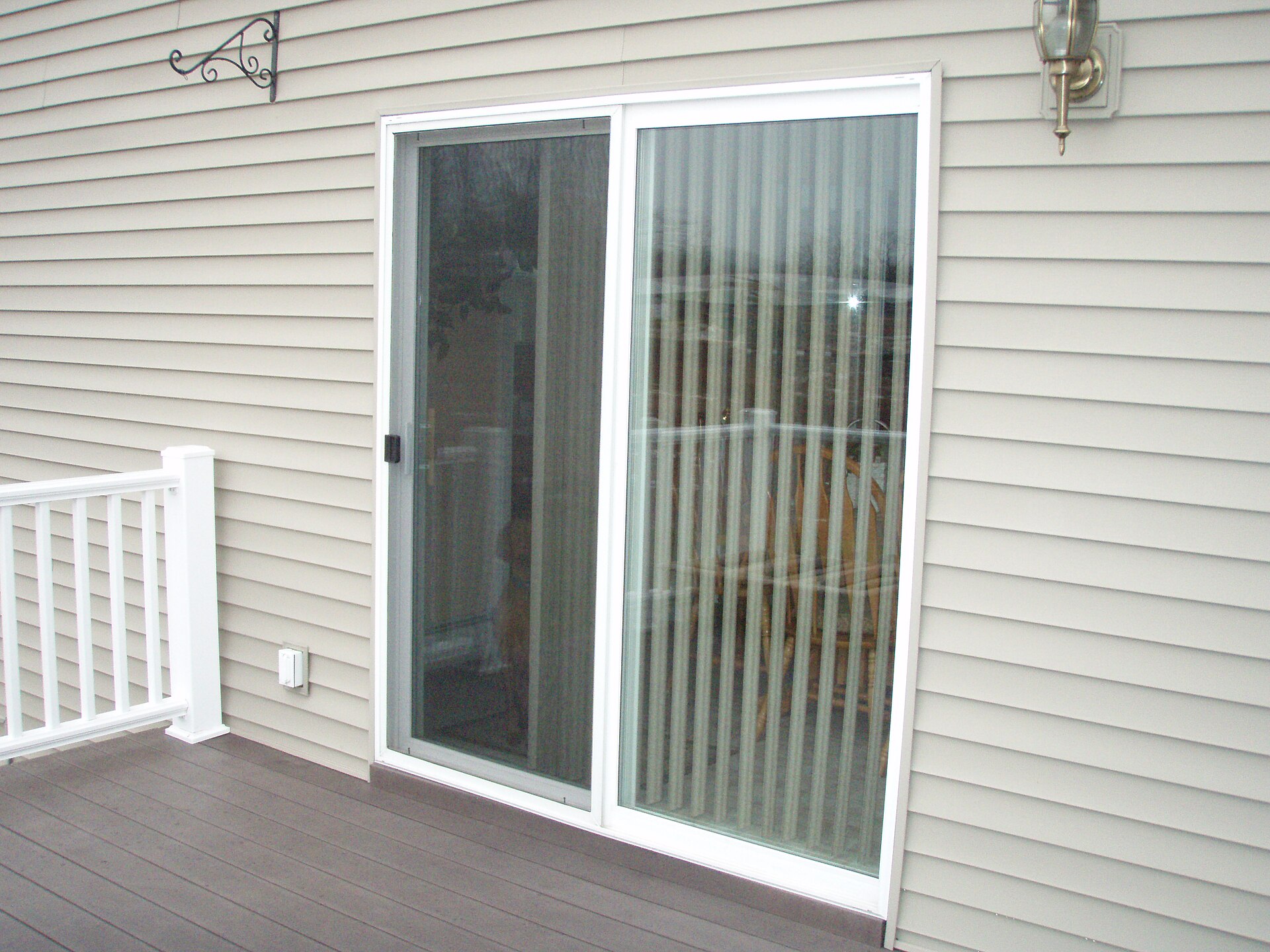 White vinyl sliding patio door set into beige siding, opening onto a deck with a white railing