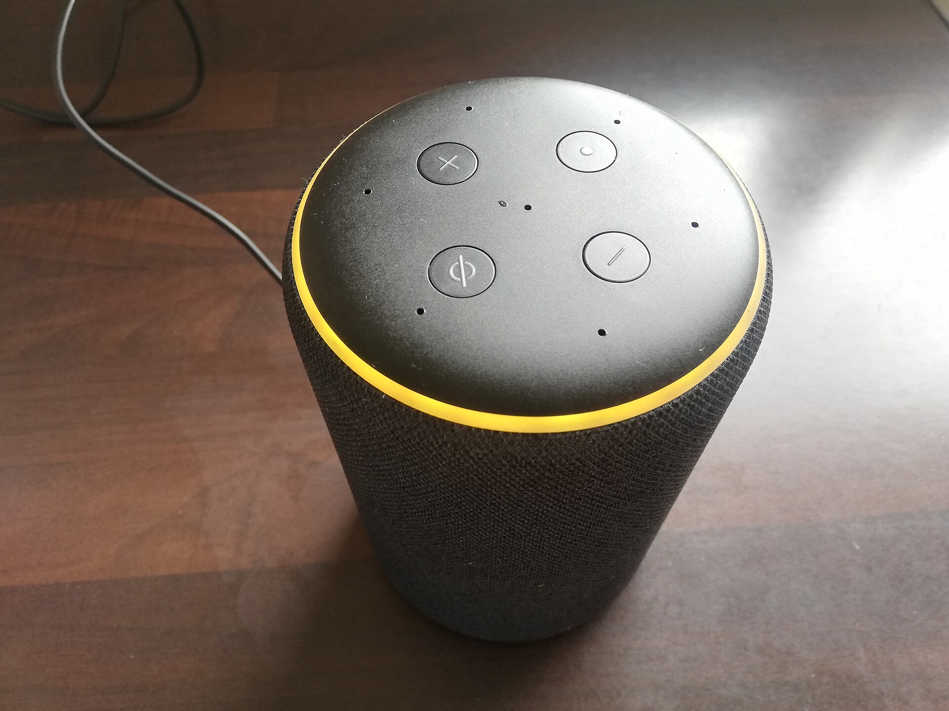 Cylindrical smart speaker with a glowing light ring sitting on a wooden table