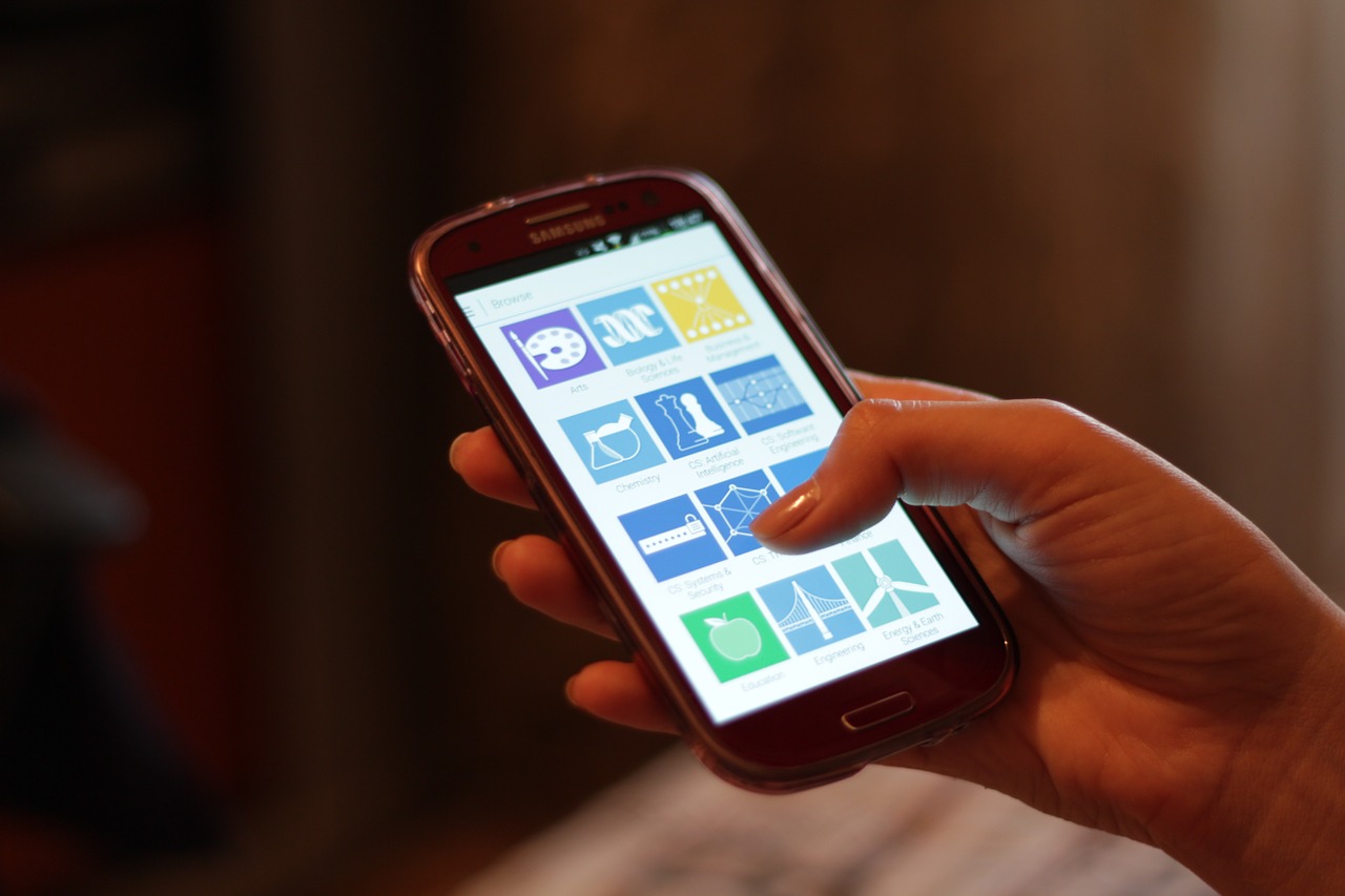 Hand holding a smartphone showing a screen of app icons against a dark background