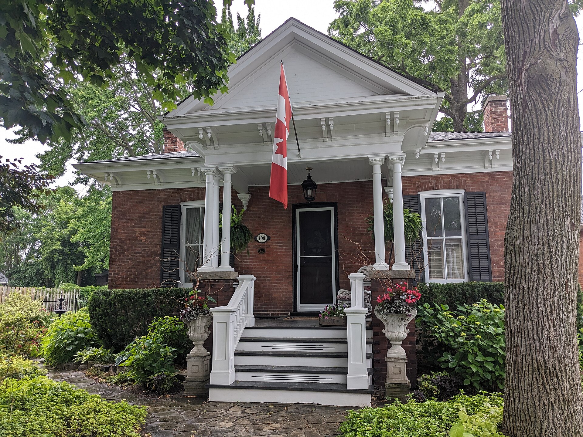 Brick house with a covered front porch, gardens and a Canadian flag in St. Catharines, Ontario