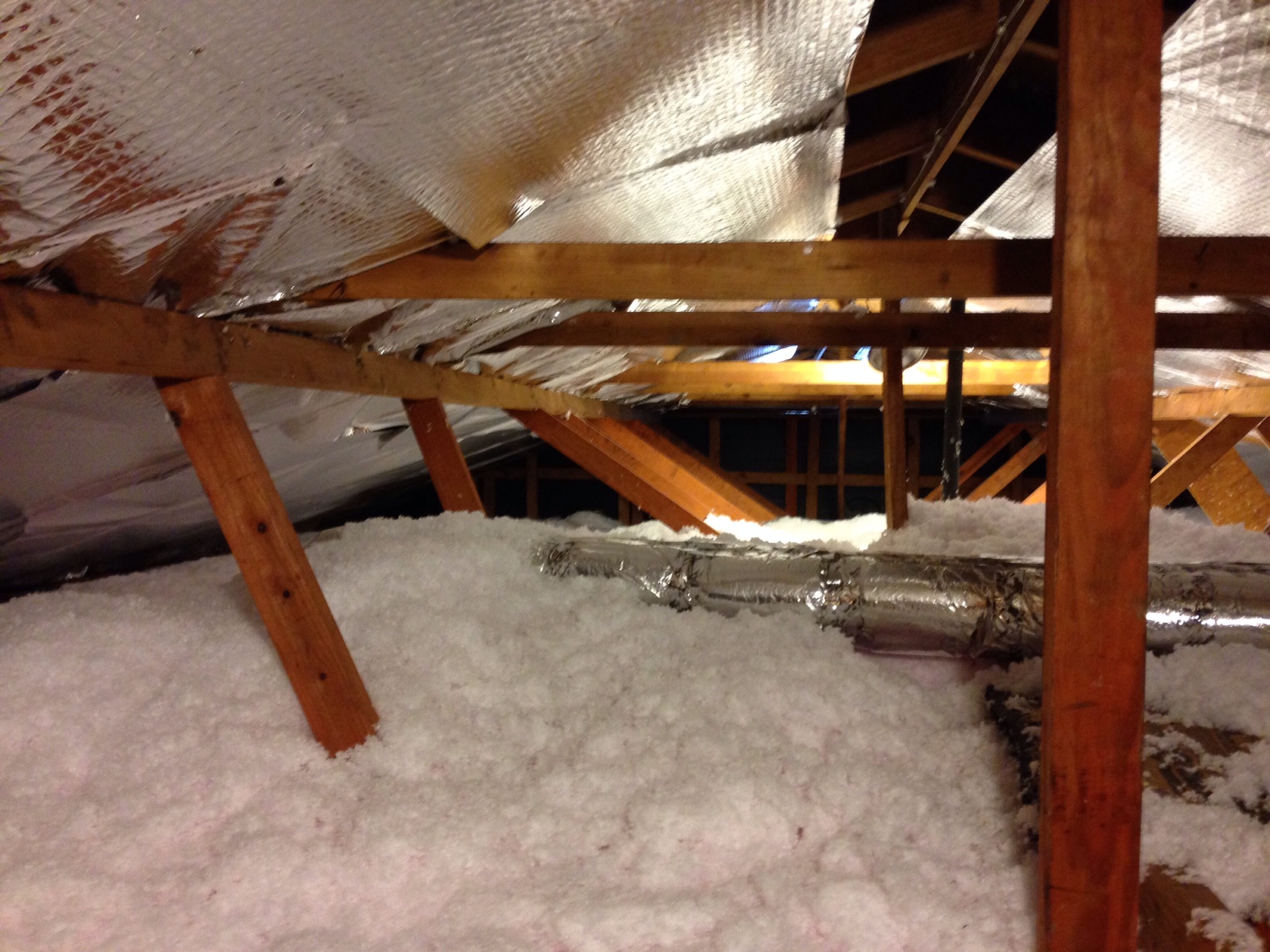 Attic with thick blown-in insulation between wooden roof rafters and insulated ductwork