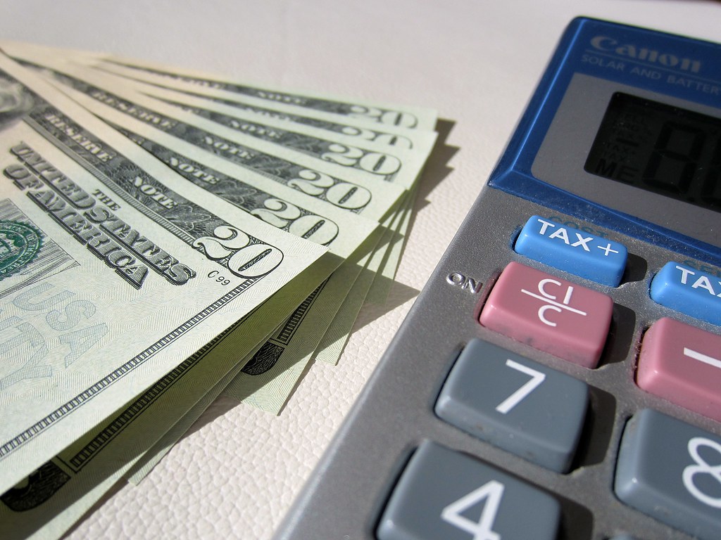 Close-up of a desk calculator beside a fanned stack of twenty-dollar banknotes