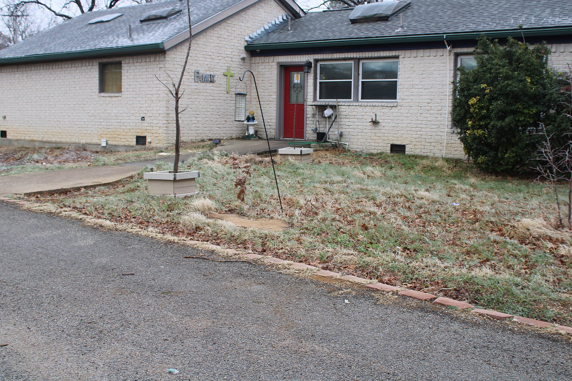 Dated single-storey ranch-style house with a red front door, shrubs and a gravel driveway