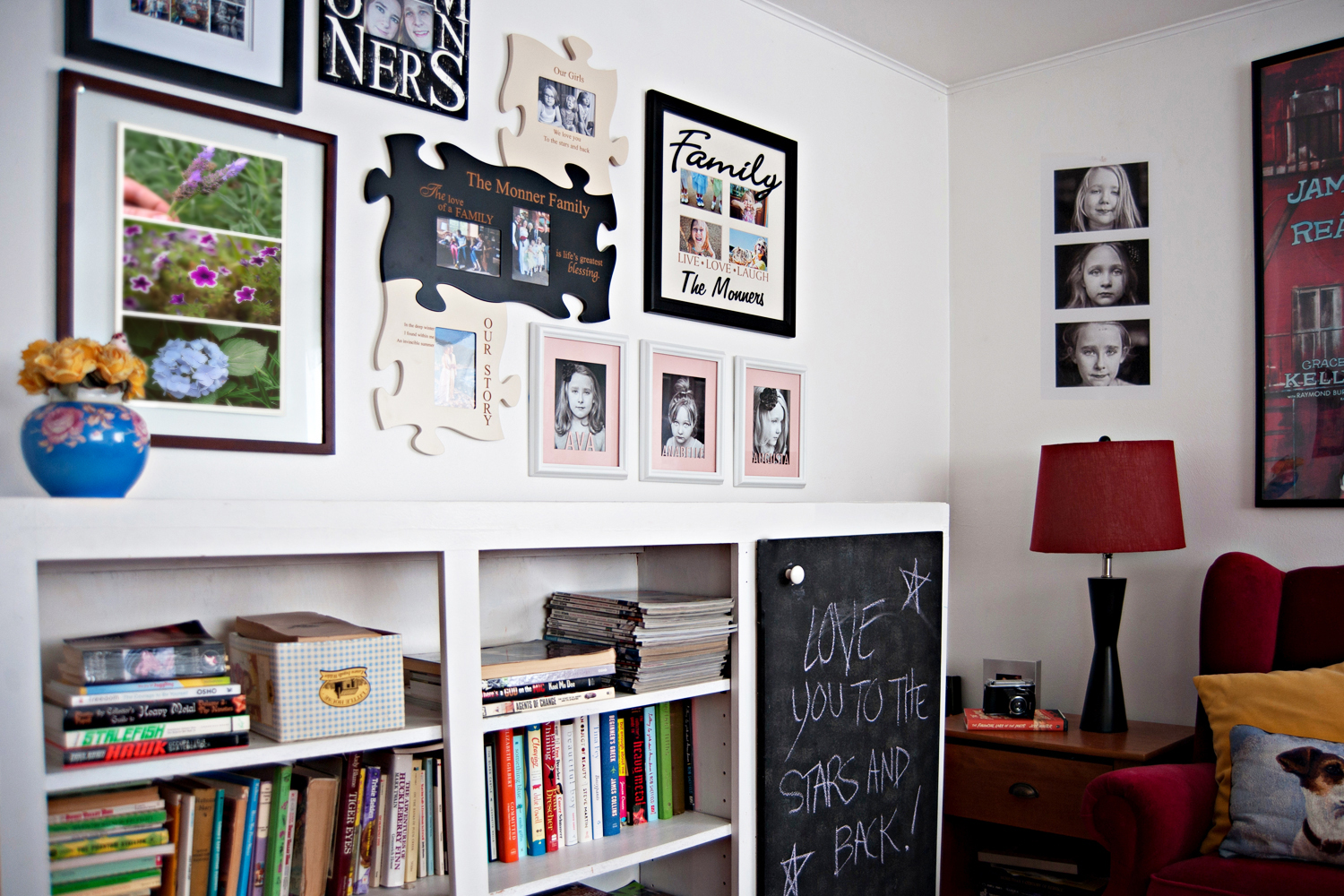 Gallery wall of framed family photos and word art above a white bookcase beside a red lamp