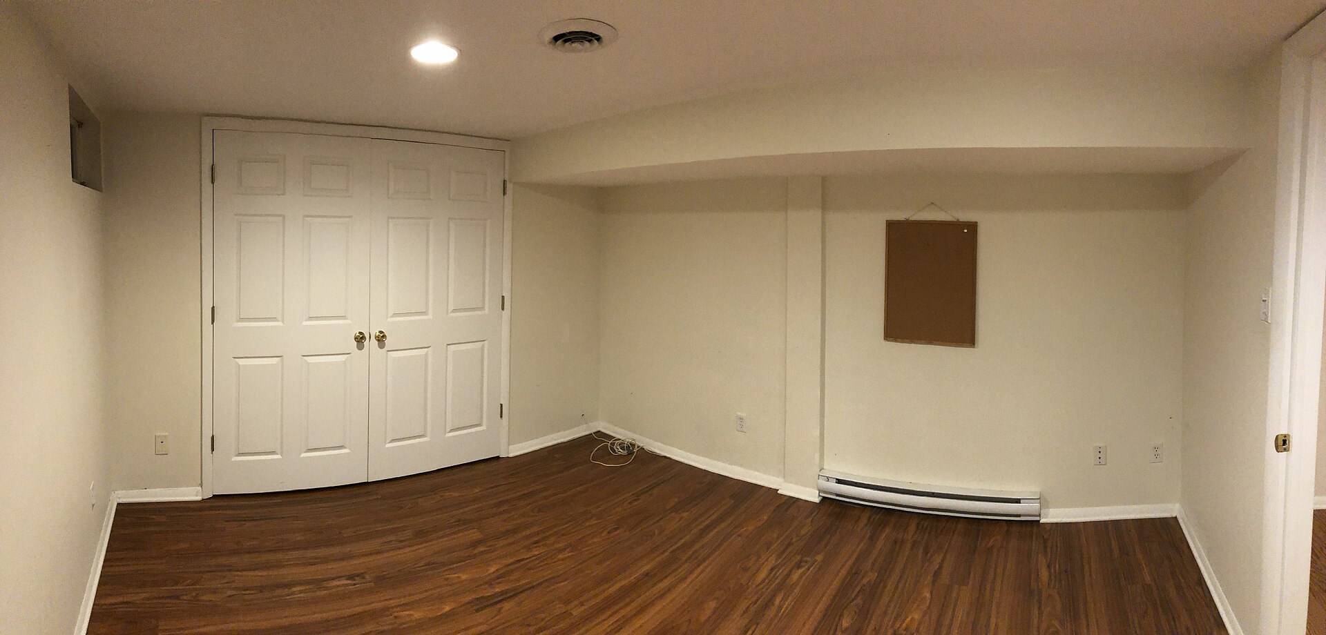 Empty finished basement room with hardwood floor, white walls, closet doors and pot lights