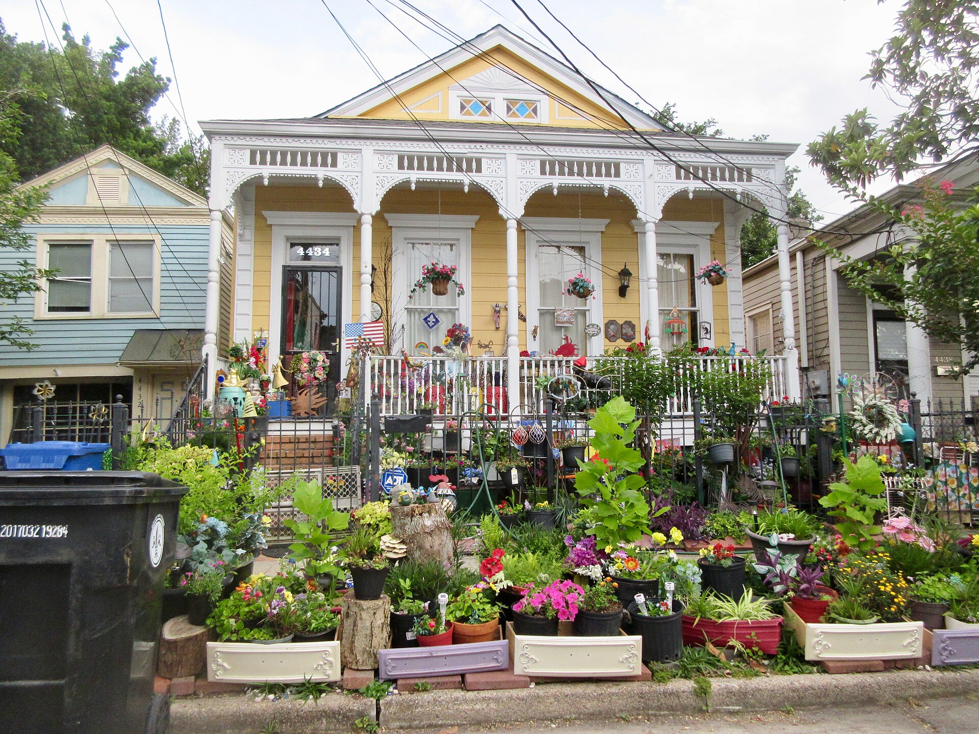 Single-storey wooden house with a front porch and a yard packed with colourful potted plants and flowers