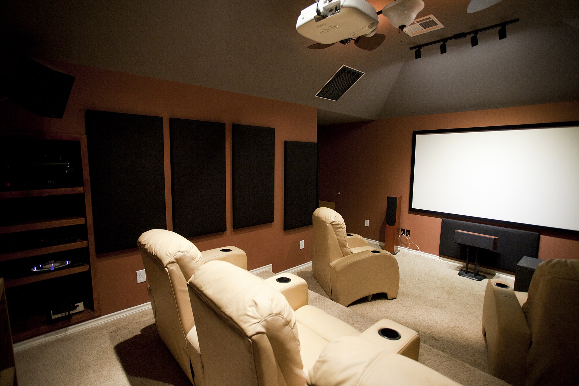 Dedicated home theatre room with a ceiling-mounted projector, large screen and leather recliners