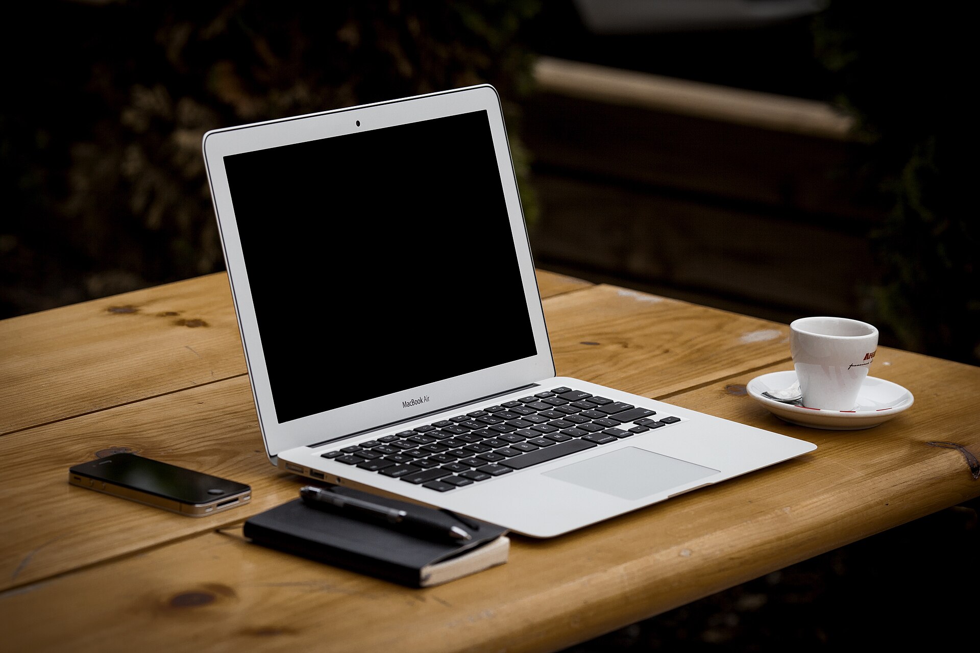 Open laptop on a wooden table beside a coffee cup, phone and notebook