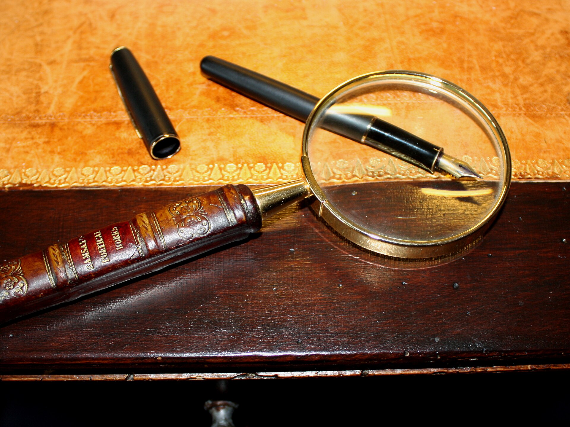 Round magnifying glass and two fountain pens resting on a dark wooden table