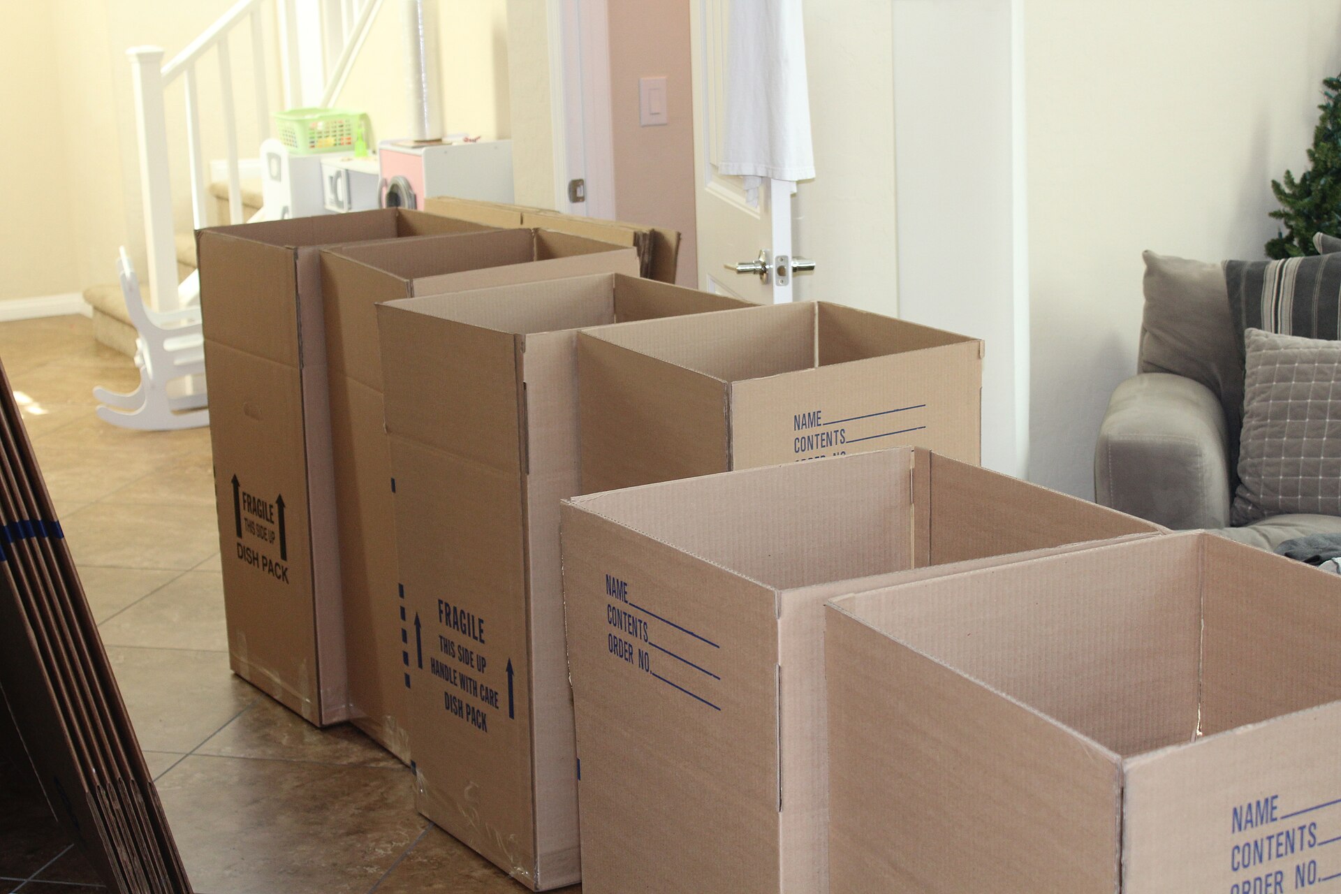 Row of open cardboard moving boxes lined up across a bright living room floor