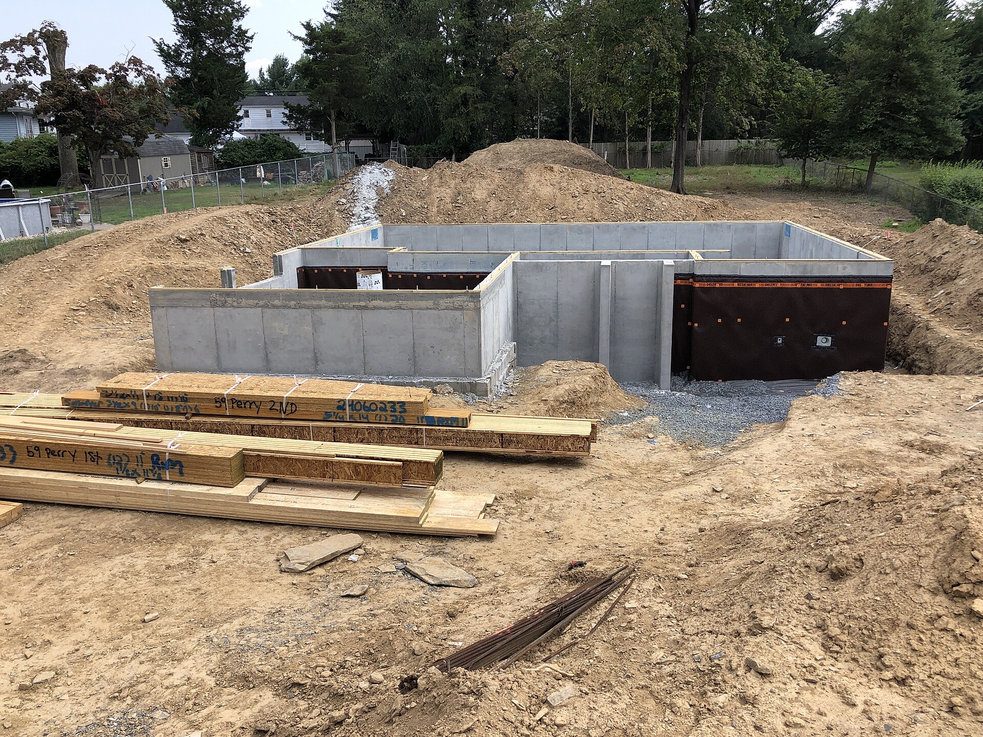 Freshly poured concrete foundation walls of a new house on a dirt lot with stacked lumber in front