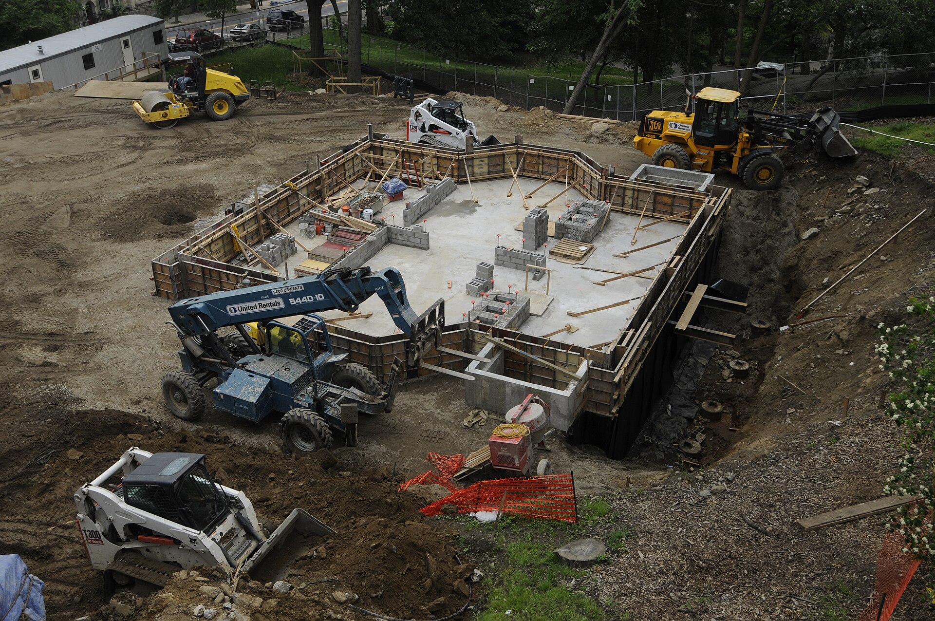 New concrete foundation in an excavated lot surrounded by construction equipment