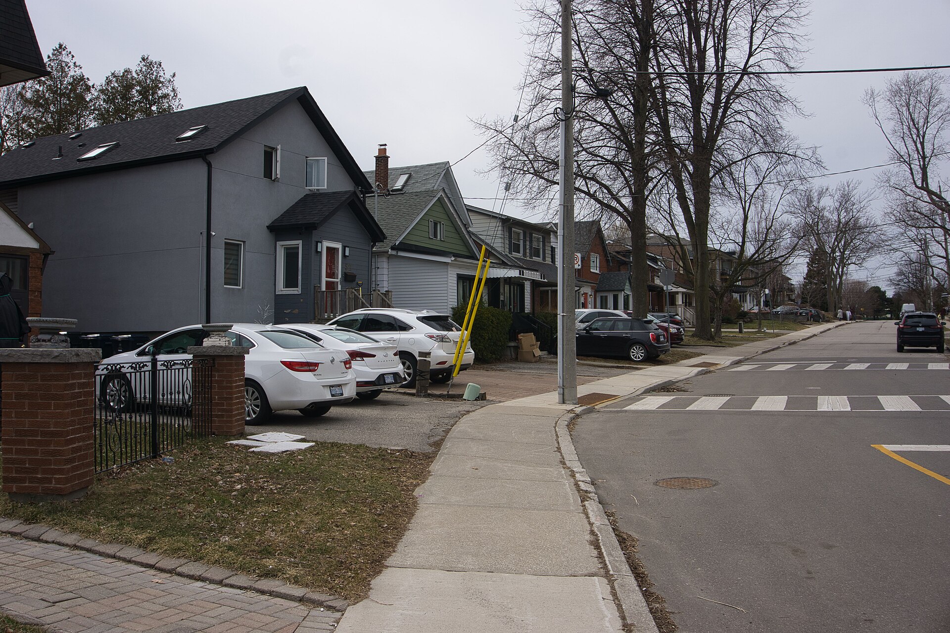 Residential street in Toronto with detached houses, parked cars, sidewalk and bare trees