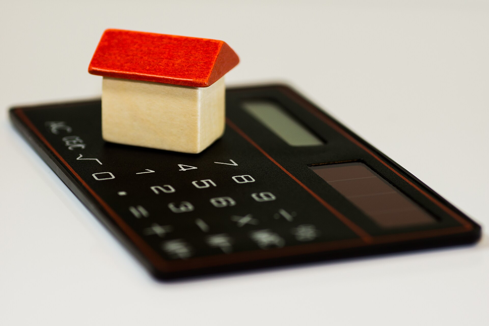 Small wooden toy house with a red roof sitting on a black calculator