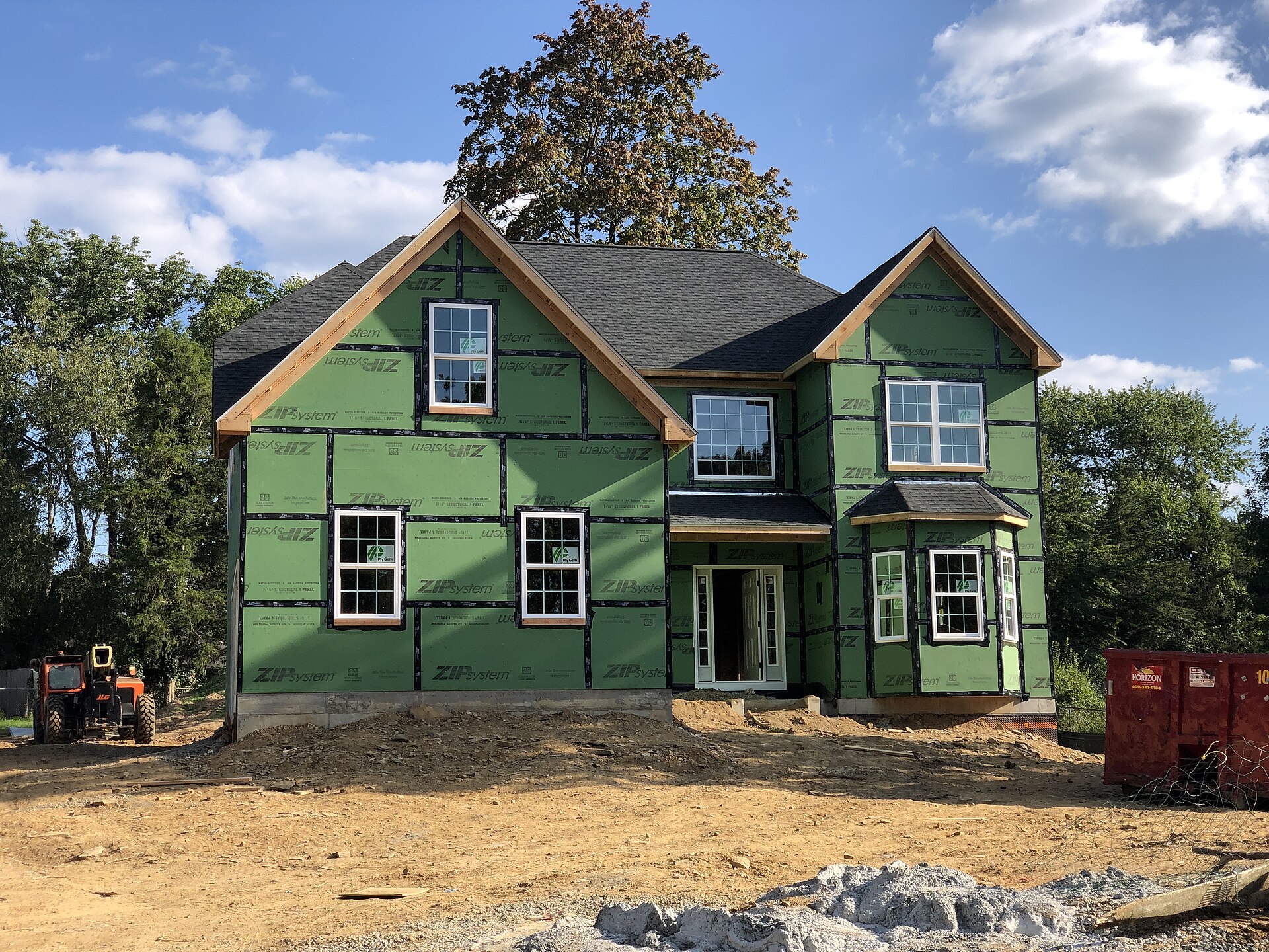 Two-storey wood-frame house under construction with green exterior sheathing and a dirt yard