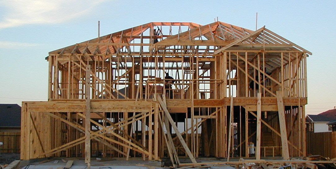 Two-storey wood-framed house under construction with exposed studs and roof trusses