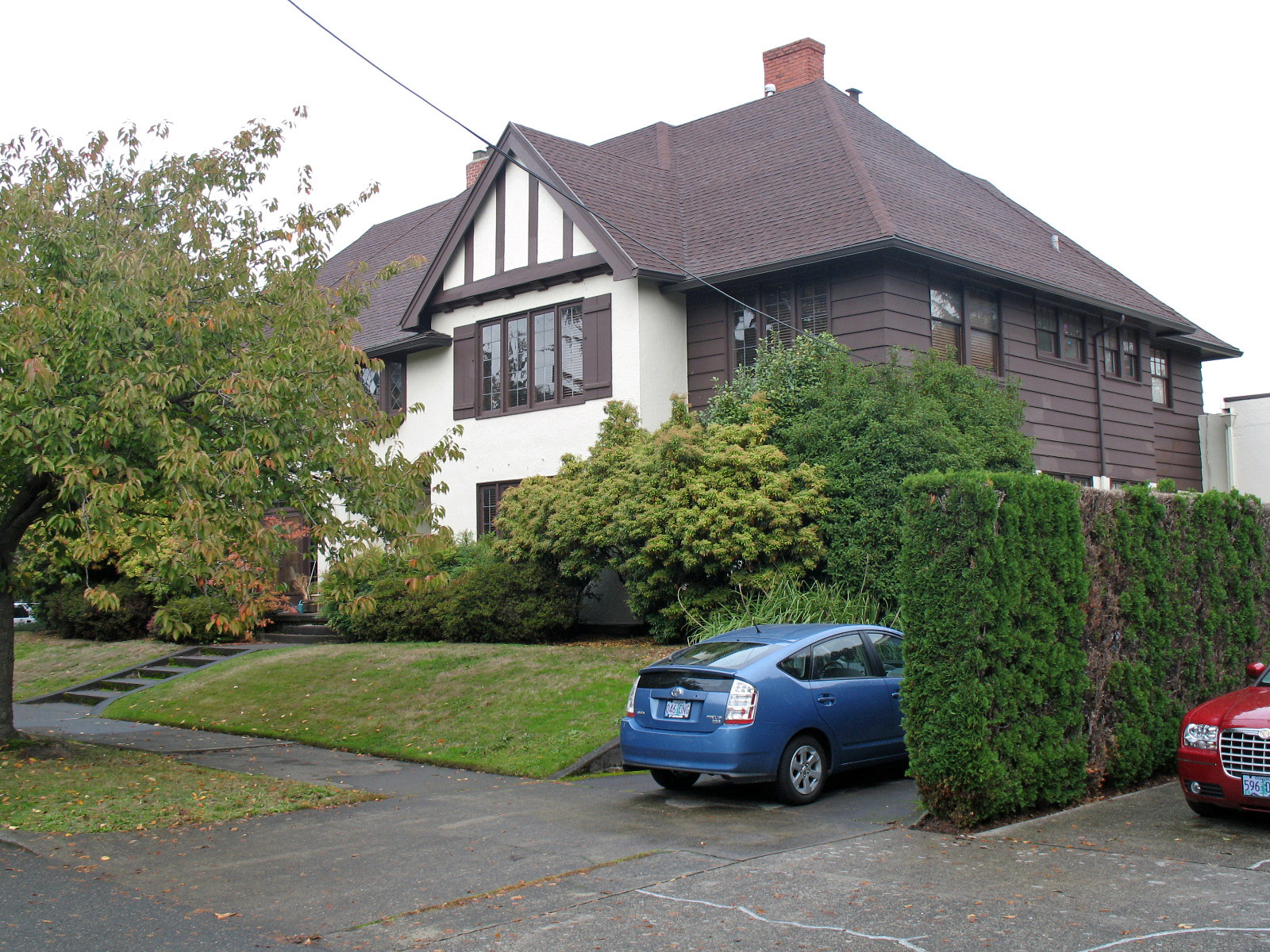 Large two-storey stucco and brick fourplex that looks like a single big house, with a front lawn and hedges